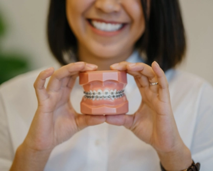 Dental model of teeth with braces, held by smiling woman.