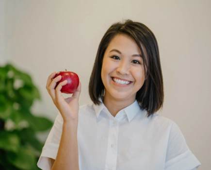 Smiling woman in white blouse holding an apple.