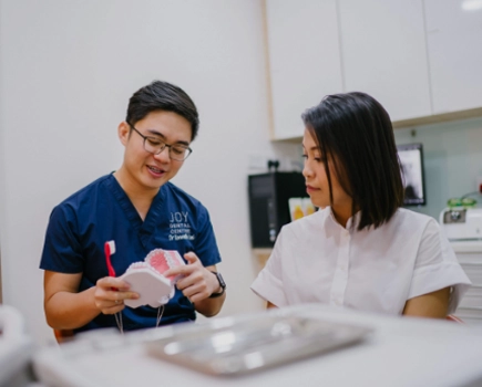 Dentist discusses with patient, holding teeth model and toothbrush.