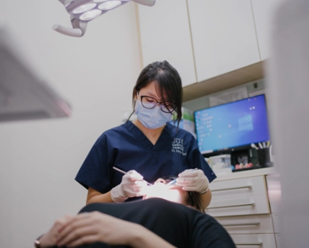 Female dentist in mask and glasses operates on patient lying in dental chair.