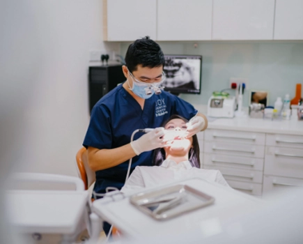 Dentist in sanitary mask operates on patient in dental chair in office.