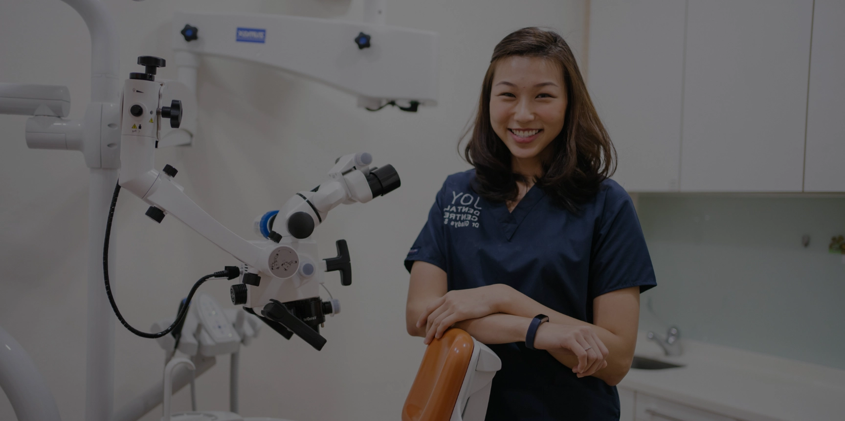 Smiling dentist posing next to dental chair and related dental equipment in office promoting children dentistry.