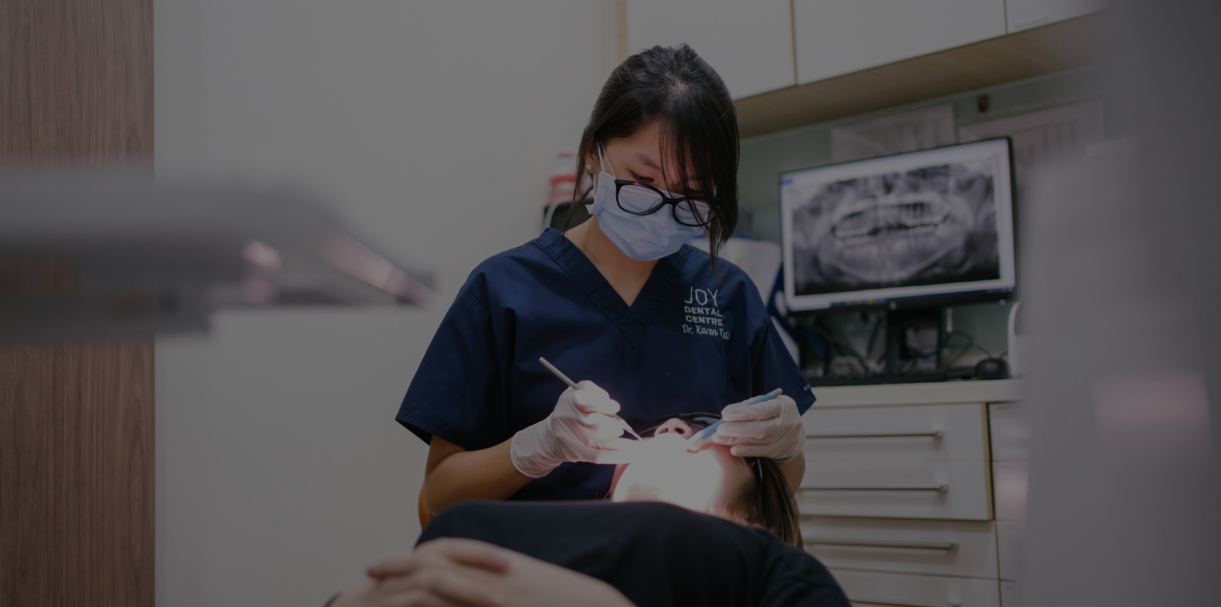 Female dentist in mask and glasses operates on patient lying in dental chair.