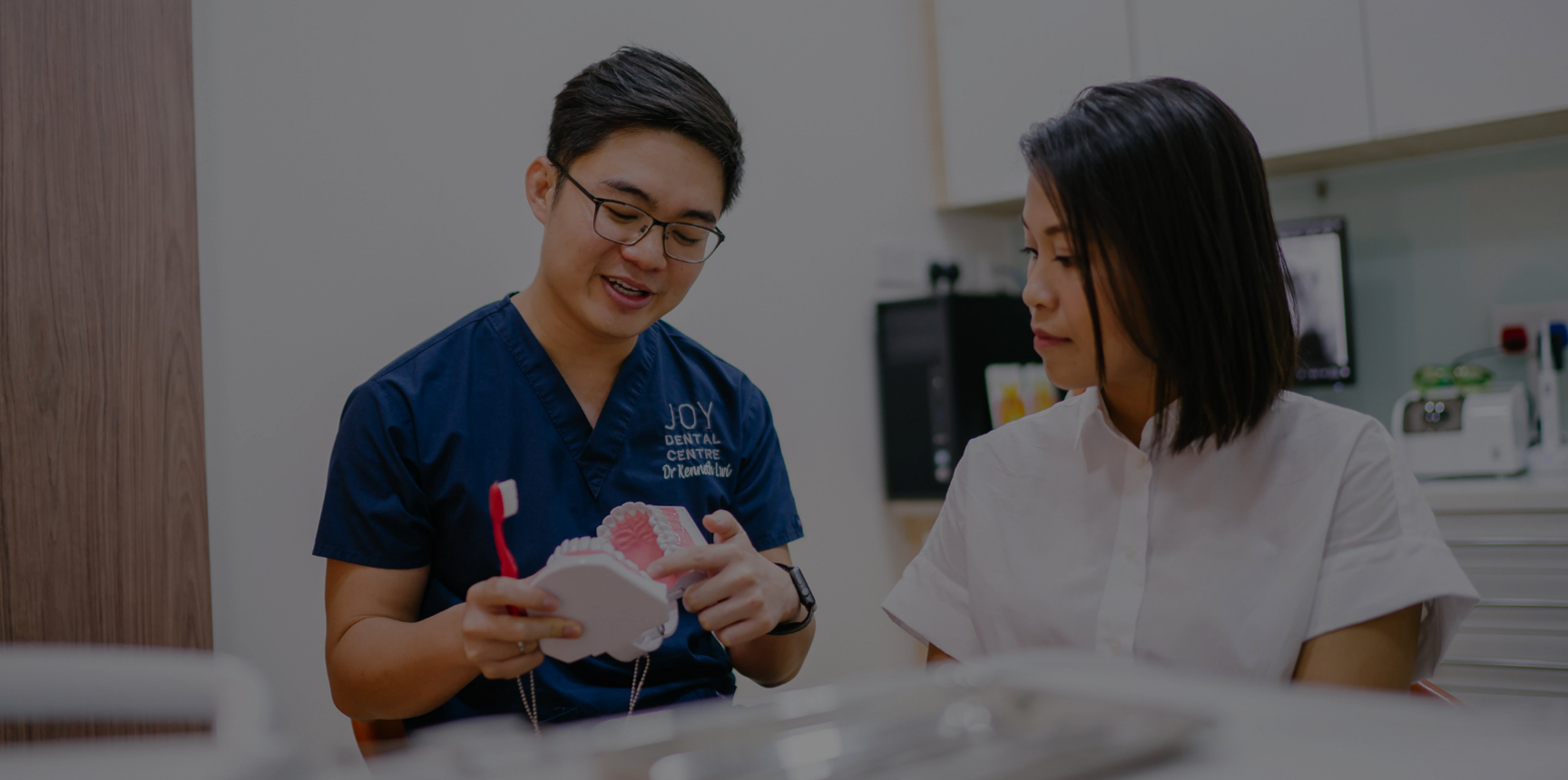 Dentist discusses with patient, holding teeth model and toothbrush.