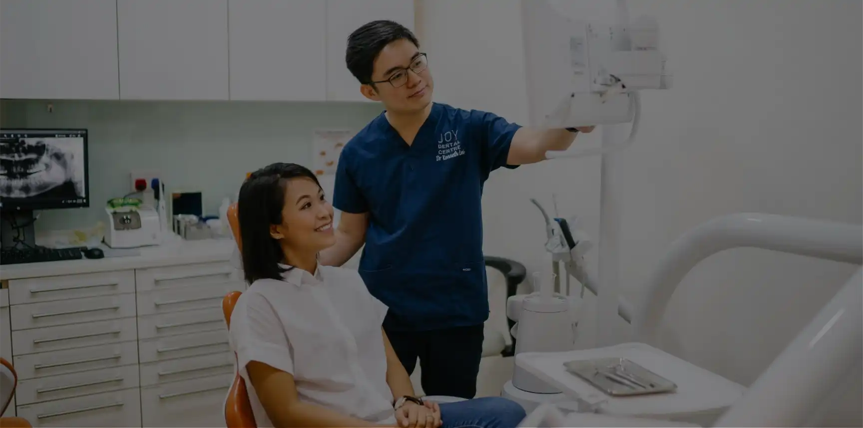 Dentist explaining information on a screen to patient sitting in dental chair.