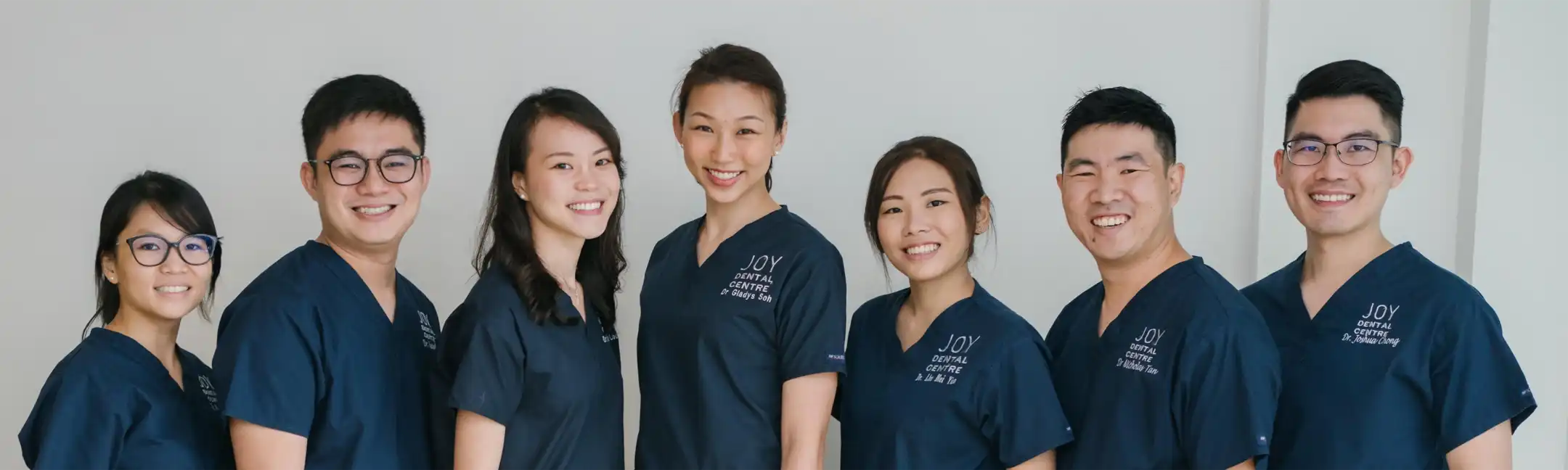 Group portrait: seven Joy Dental Centre staff, smiling in navy uniforms in lineup.