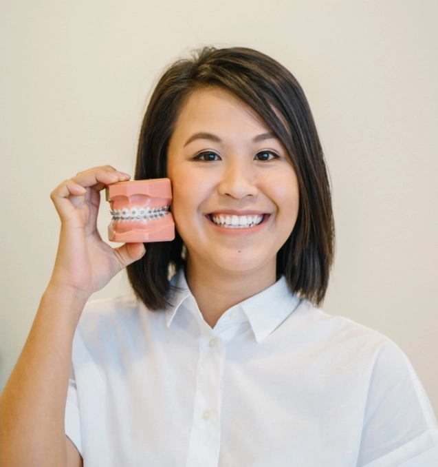 Dental model of teeth with braces, held by smiling woman.