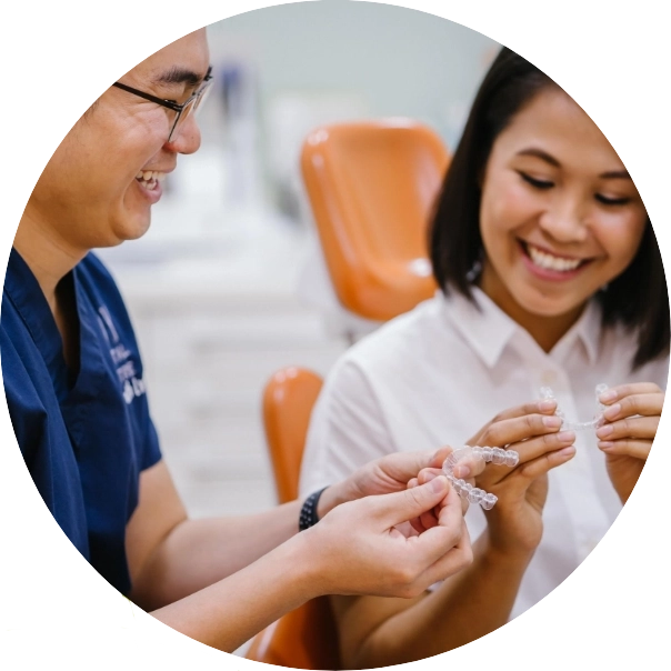 Dentist discusses with patient, holding a model of Invisalign aligners.