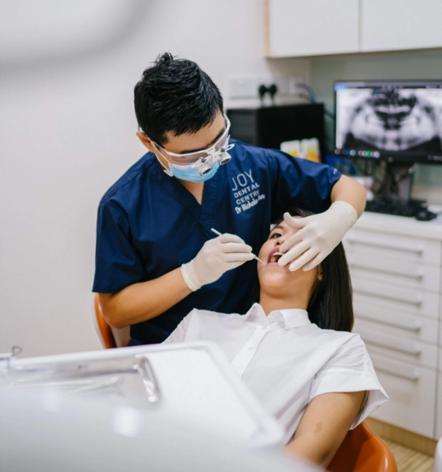 Male dentist in mask and glasses operates on patient lying in dental chair.