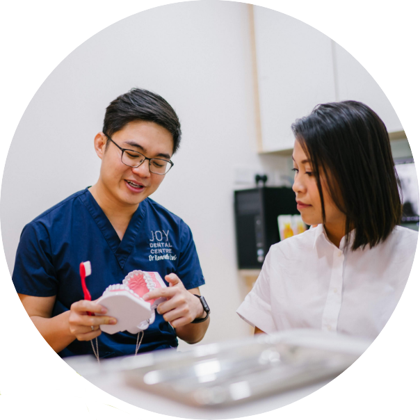 Dentist discusses with patient, holding teeth model and toothbrush.