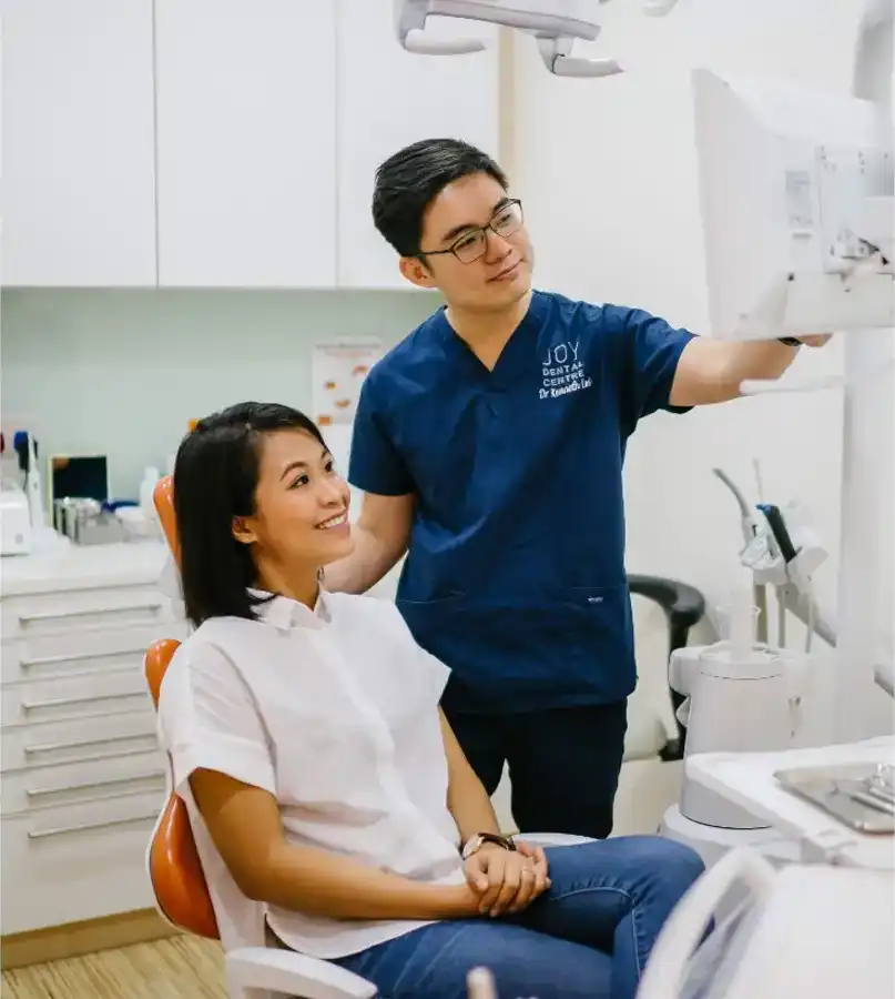 Dentist explaining information on a screen to patient sitting in dental chair.