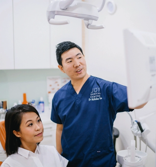 Dentist explaining a root canal on a screen to patient sitting in dental chair.