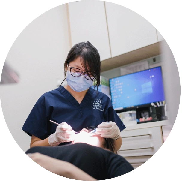 Female dentist in mask and glasses performing a root canal on patient lying in dental chair.