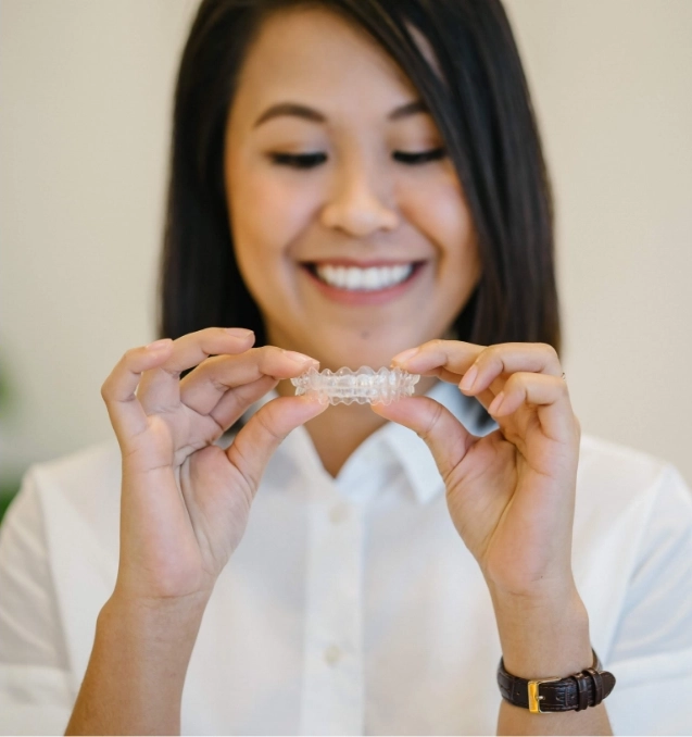 Invisalign aligners model, held by smiling woman.